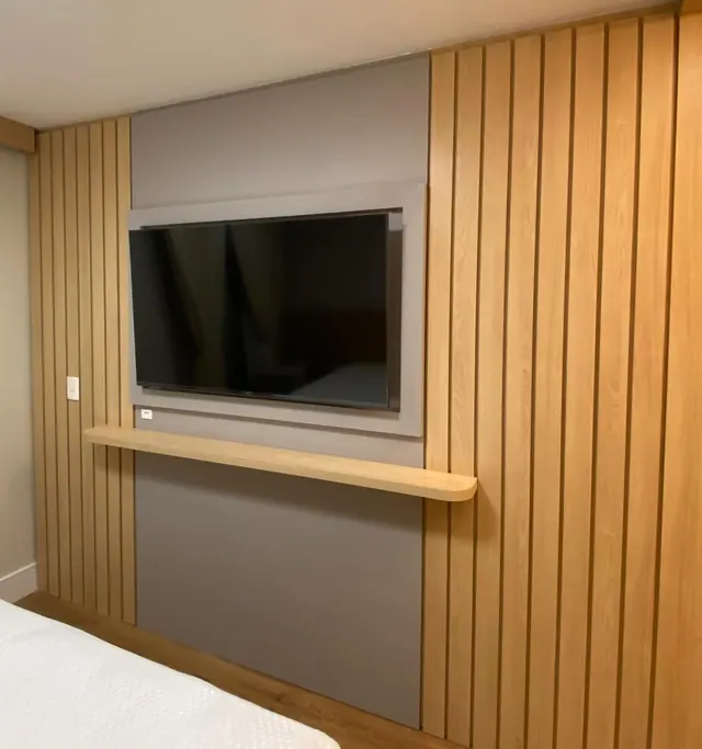Dormitório com painel ripado em madeira, suporte de TV e prateleira suspensa